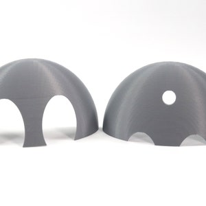 May include: Two gray 3D printed plastic hemispheres with cutouts. One hemisphere has two large cutouts and the other has three smaller cutouts and a single round hole.
