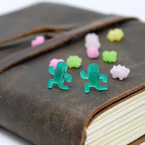 May include: Two green plastic figurines of people running, placed on a brown leather-bound journal with colorful candy sprinkles scattered around them.