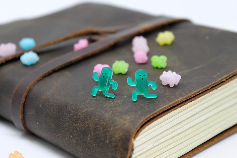 May include: Two green plastic figurines of people running, placed on a brown leather-bound journal with colorful candy sprinkles scattered around them.