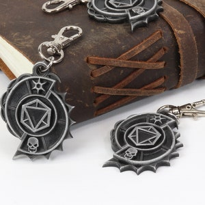 May include: Two silver metal keychains with a skull and a dice design. The keychains are hanging from a brown leather journal.