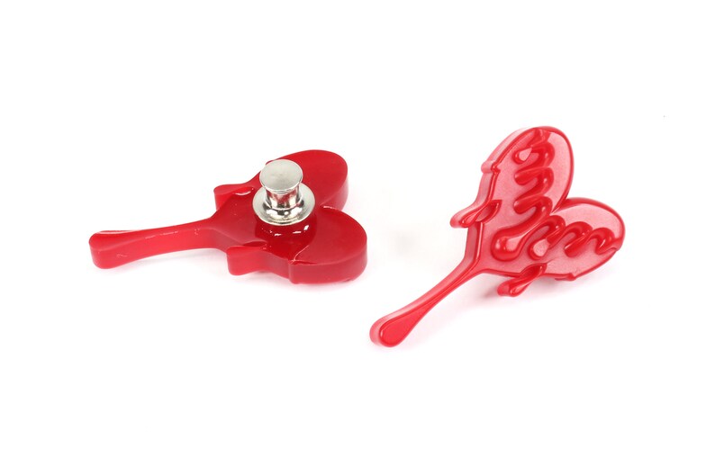 May include: Two red plastic heart-shaped buttons with a metal pin on one. The heart on the left has a raised design and the heart on the right has the word "Love" written in a script font.