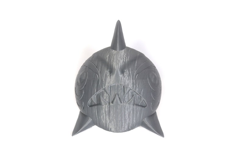 May include: A gray 3D printed shark head with a toothy grin and carved details. The shark head is a decorative object.