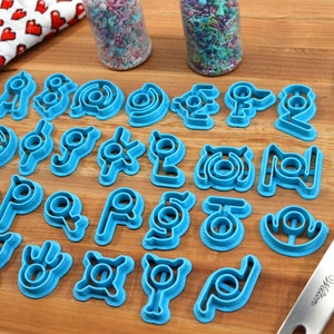 May include: A set of 20 blue plastic cookie cutters shaped like different symbols. The cutters are arranged in four rows on a wooden surface.