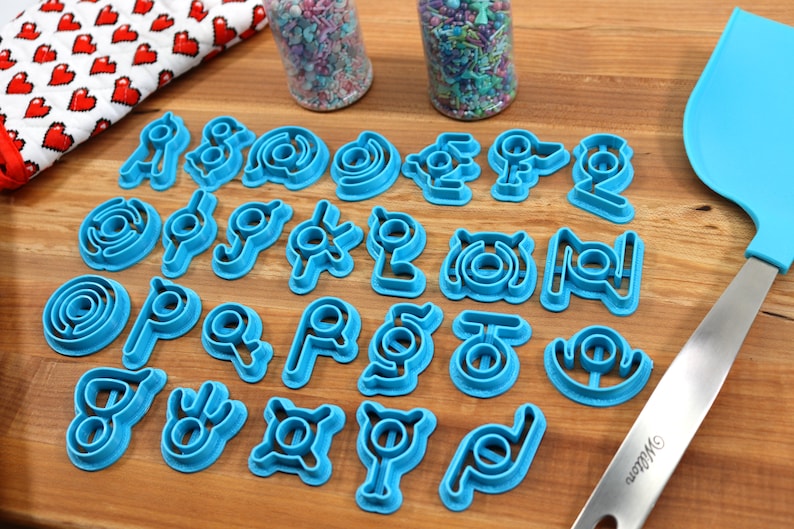 May include: A set of 20 blue plastic cookie cutters shaped like different symbols. The cutters are arranged in four rows on a wooden surface.