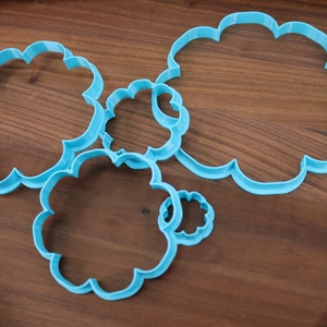 May include: A set of five blue plastic cookie cutters shaped like clouds, arranged on a wooden surface.