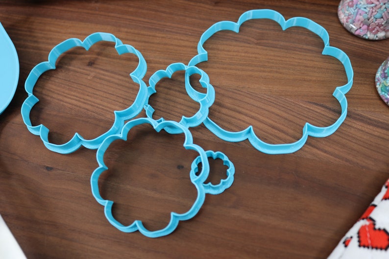 May include: A set of five blue plastic cookie cutters shaped like clouds, arranged on a wooden surface.