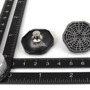 May include: A black metal ruler with a silver knob and two black metal pieces with a geometric design. The ruler has markings in inches.