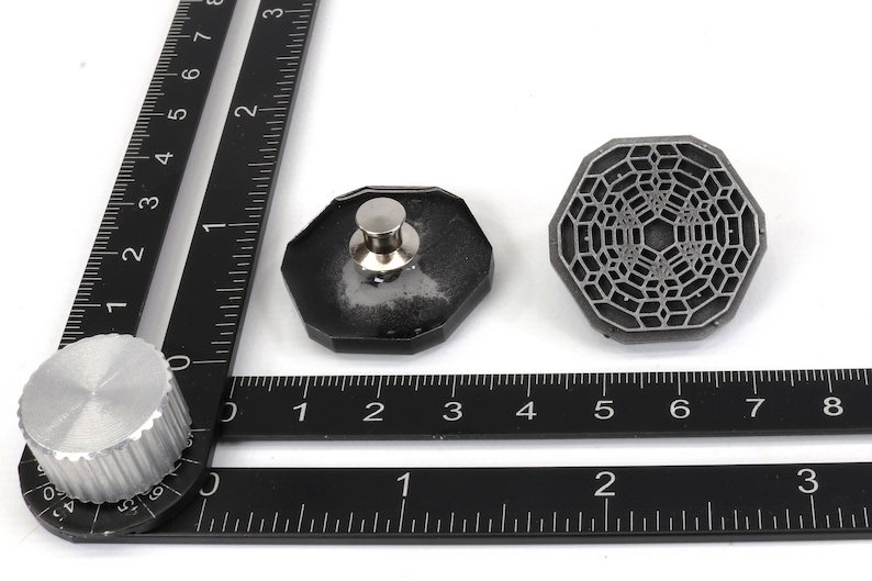 May include: A black metal ruler with a silver knob and two black metal pieces with a geometric design. The ruler has markings in inches.
