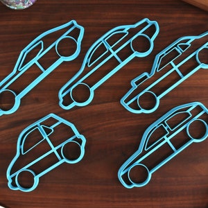 May include: Five blue plastic cookie cutters shaped like different cars. The cutters are on a wooden surface.