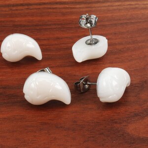 May include: Four white shell earrings with silver posts. The earrings are shaped like a crescent moon.