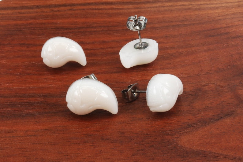 May include: Four white shell earrings with silver posts. The earrings are shaped like a crescent moon.
