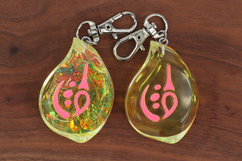 May include: Two teardrop-shaped keychains with a pink symbol inside. One keychain is clear yellow and the other is iridescent.