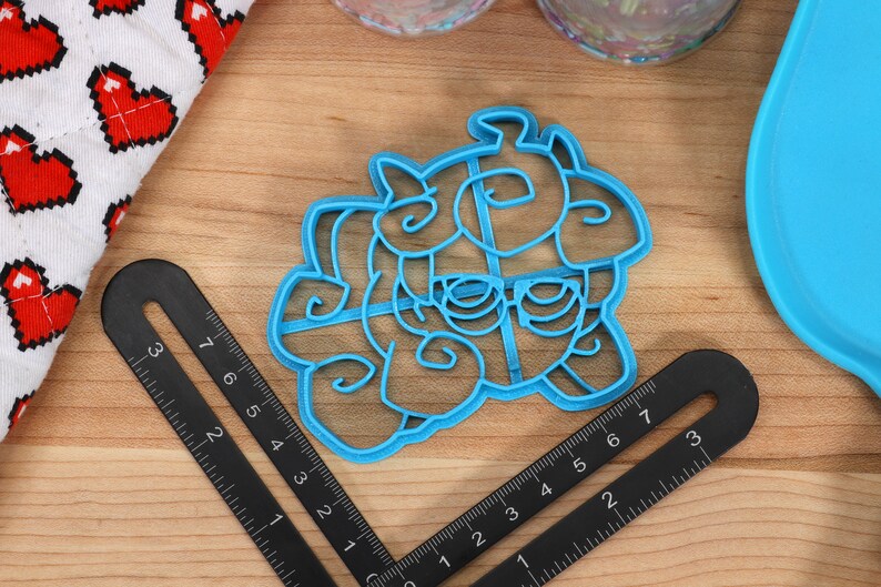 May include: A blue plastic cookie cutter shaped like a cartoon unicorn with a horn, mane, and tail. The cutter is on a wooden surface with a ruler.