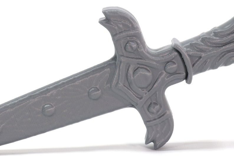 May include: A gray plastic sword with a detailed handle and a sharp point. The sword has a textured surface and a decorative design on the handle.