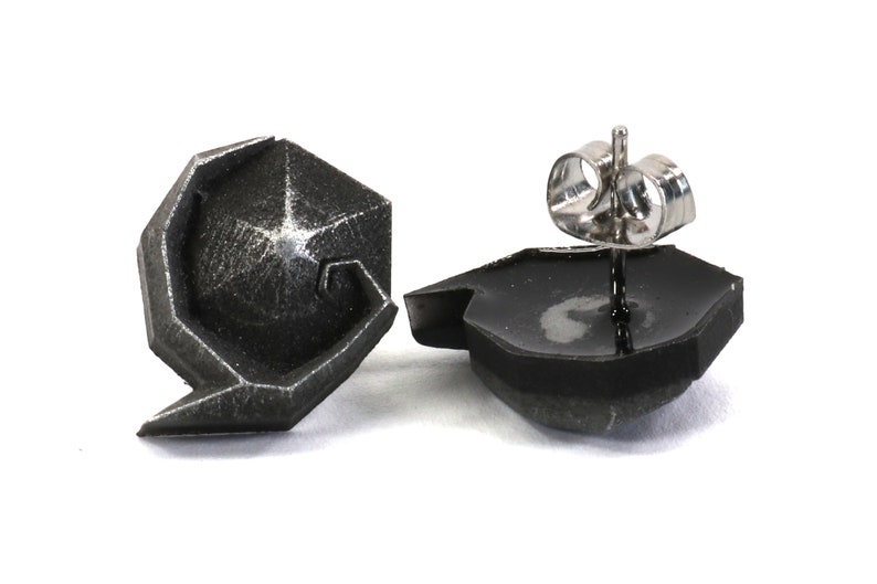 May include: A pair of silver geometric stud earrings. The earrings are made of a textured metal and have a unique, modern design.
