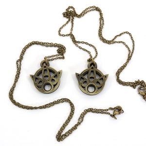 May include: Two gold-toned necklaces with intricate, circular pendants. Each pendant features a geometric design with a central hole.