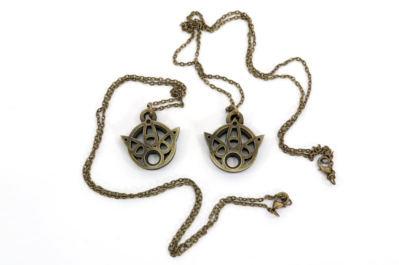May include: Two gold-toned necklaces with intricate, circular pendants. Each pendant features a geometric design with a central hole.
