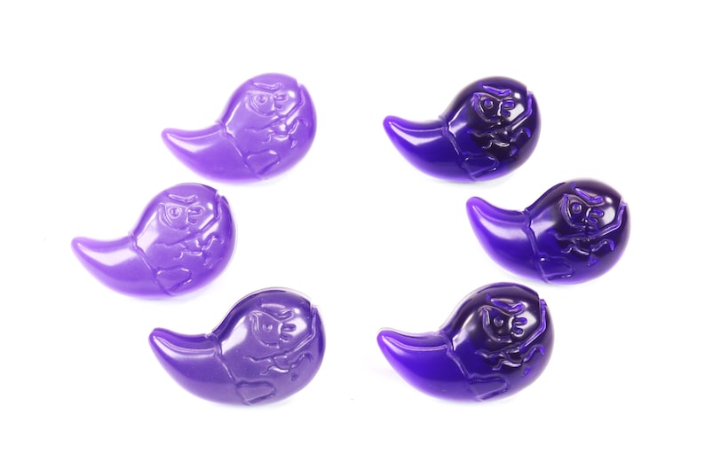 K&ouml;nnte beinhalten: Sechs violette, geisterf&ouml;rmige Perlen mit einem erhabenen Design. Die Perlen sind aus Glas oder Kunststoff und haben eine gl&auml;nzende Oberfl&auml;che.