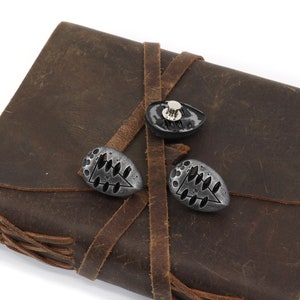 May include: A brown leather journal with three metal clasps. The clasps are oval shaped and have a tree design.