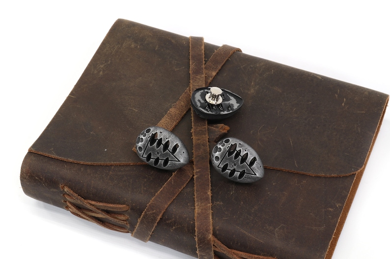 May include: A brown leather journal with three metal clasps. The clasps are oval shaped and have a tree design.