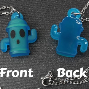 May include: A blue translucent necklace with a cactus-shaped pendant. The front of the pendant has a cartoon face with black eyes and a surprised expression. The back of the pendant is plain. The necklace is made of a silver chain.