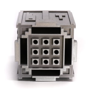 May include: A silver metal box with a grid of nine round holes on the front. The box has a textured surface and appears to be made of a 3D printed material.