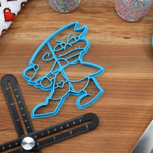 Puede incluir: Un cortador de galletas de pl&aacute;stico azul con forma de personaje de dibujos animados con un sombrero y una expresi&oacute;n de enfado.