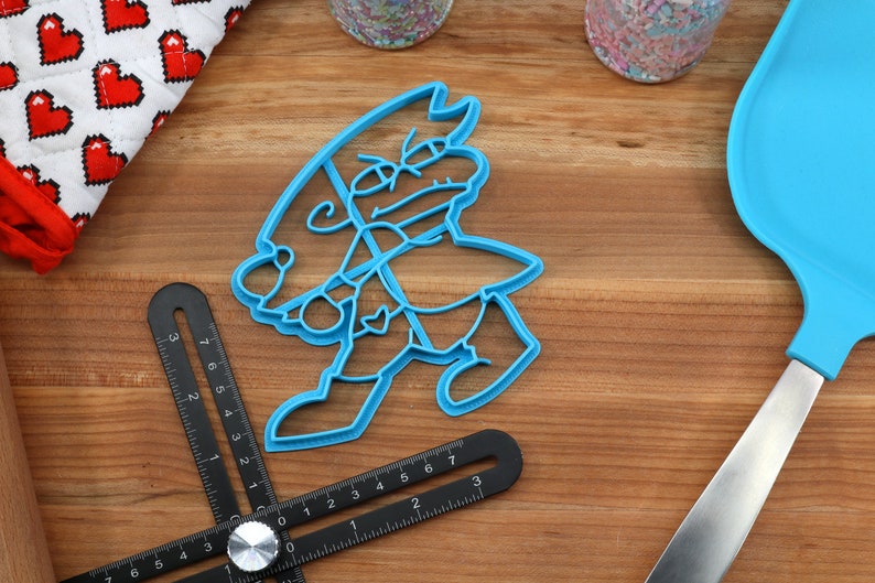Puede incluir: Un cortador de galletas de pl&aacute;stico azul con forma de personaje de dibujos animados con un sombrero y una expresi&oacute;n de enfado.