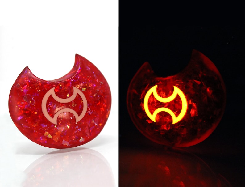 May include: A red crescent moon-shaped resin pendant with a white symbol inside. The pendant glows in the dark, revealing a yellow symbol.