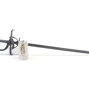 May include: A black metal sword with an ornate handle and a long, straight blade. A can of drink is placed next to the sword for scale.