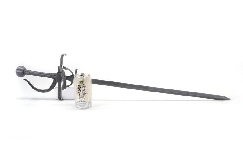 May include: A black metal sword with an ornate handle and a long, straight blade. A can of drink is placed next to the sword for scale.