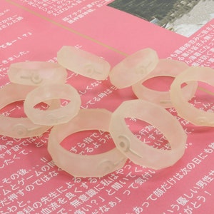 May include: A close-up of a group of clear plastic rings with numbers printed on them. The rings are scattered on a pink surface.