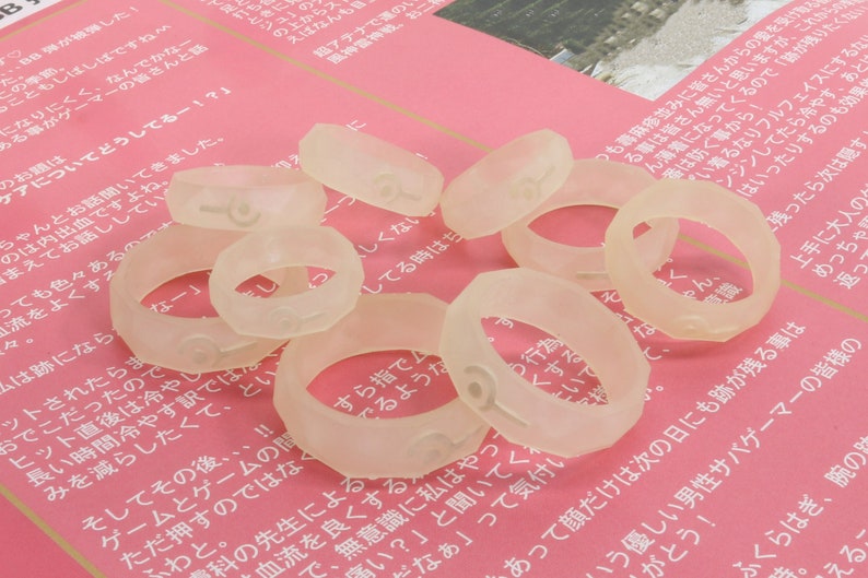 May include: A close-up of a group of clear plastic rings with numbers printed on them. The rings are scattered on a pink surface.