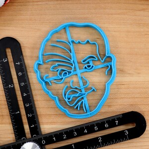 May include: A blue plastic cookie cutter shaped like a person's face. The face has a detailed design with lines and wrinkles.