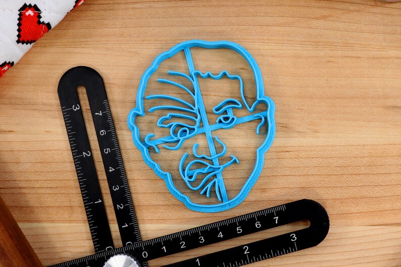 May include: A blue plastic cookie cutter shaped like a person's face. The face has a detailed design with lines and wrinkles.