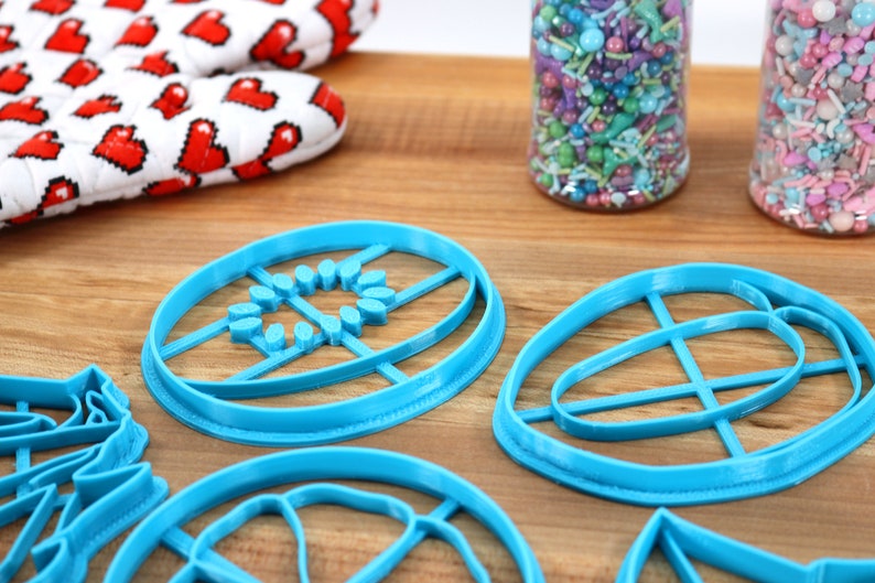 May include: A set of five blue plastic cookie cutters in various shapes, including a circle, an oval, and a leaf. The cutters are on a wooden surface.