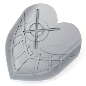 May include: A gray, heart-shaped object with a geometric design. The design includes a cross, circles, and a grid pattern. The object is made of a solid material and has a smooth surface. The background is white.