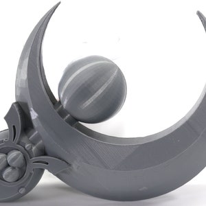 May include: A gray 3D printed crescent moon with a sphere attached to the center. The sphere has a textured surface and is surrounded by the crescent moon.