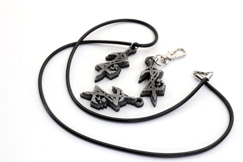 May include: A black cord necklace with three silver charms. The charms are stylized designs of the letter "Z".