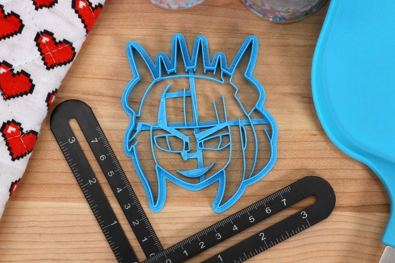 May include: A blue plastic cookie cutter shaped like a cartoon character with a crown, horns, and a mischievous expression.