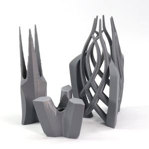 May include: Three gray 3D printed sculptures. The sculptures are abstract and have a geometric design. The sculptures are made of a smooth, matte material.