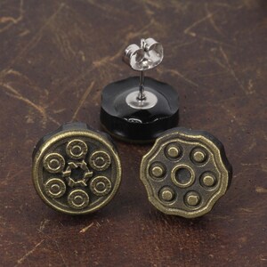 以下が含まれることがあります： アンティークスタイルのスタッドピアス3つ。銃のシリンダーのデザイン。ピアスはブロンズ色の金属と黒い裏地で作られています。1つのピアスは、ポストとバタフライバックが付いています。