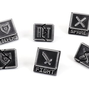 May include: Six silver-colored metal game pieces with pixelated graphics and text. The pieces are shaped like squares with rounded corners. The text on the pieces reads "DEFEND", "FIGHT", "SPARE", "ALT", and "X".