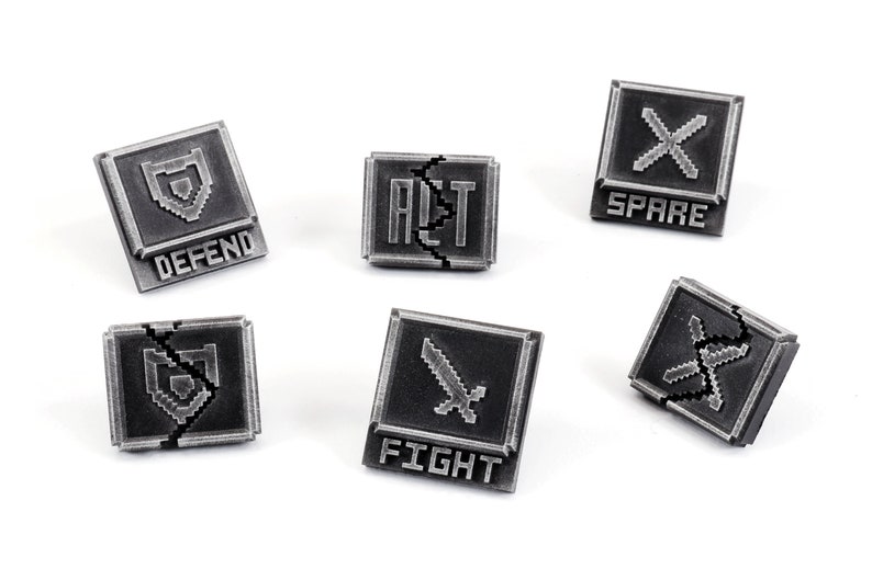 May include: Six silver-colored metal game pieces with pixelated graphics and text. The pieces are shaped like squares with rounded corners. The text on the pieces reads "DEFEND", "FIGHT", "SPARE", "ALT", and "X".
