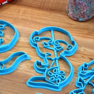 May include: A set of four blue plastic cookie cutters shaped like a skeleton holding a flower, a flower, a skeleton holding a flower, and a flower.
