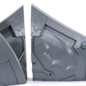 May include: Two gray, 3D printed, geometric shapes with intricate designs. The shapes are connected at the top and appear to be part of a larger structure.