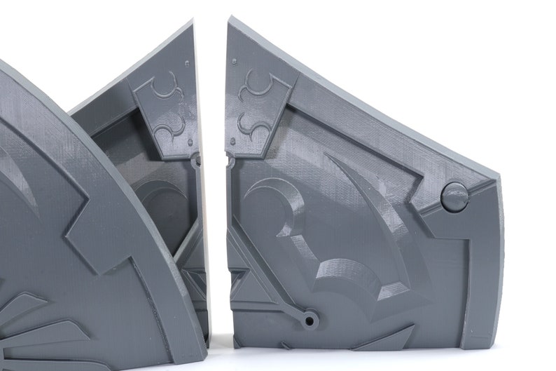 May include: Two gray, 3D printed, geometric shapes with intricate designs. The shapes are connected at the top and appear to be part of a larger structure.