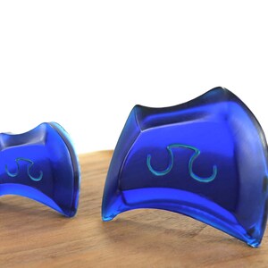 May include: Two blue glass paperweights with a wave design. The paperweights are on a wooden surface.