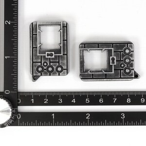 May include: Two silver-colored metal keychains with a brick pattern and a keyhole design. The keychains are about 2 inches long and 1 inch wide.