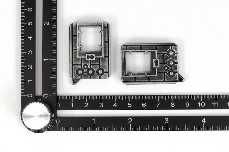 May include: Two silver-colored metal keychains with a brick pattern and a keyhole design. The keychains are about 2 inches long and 1 inch wide.